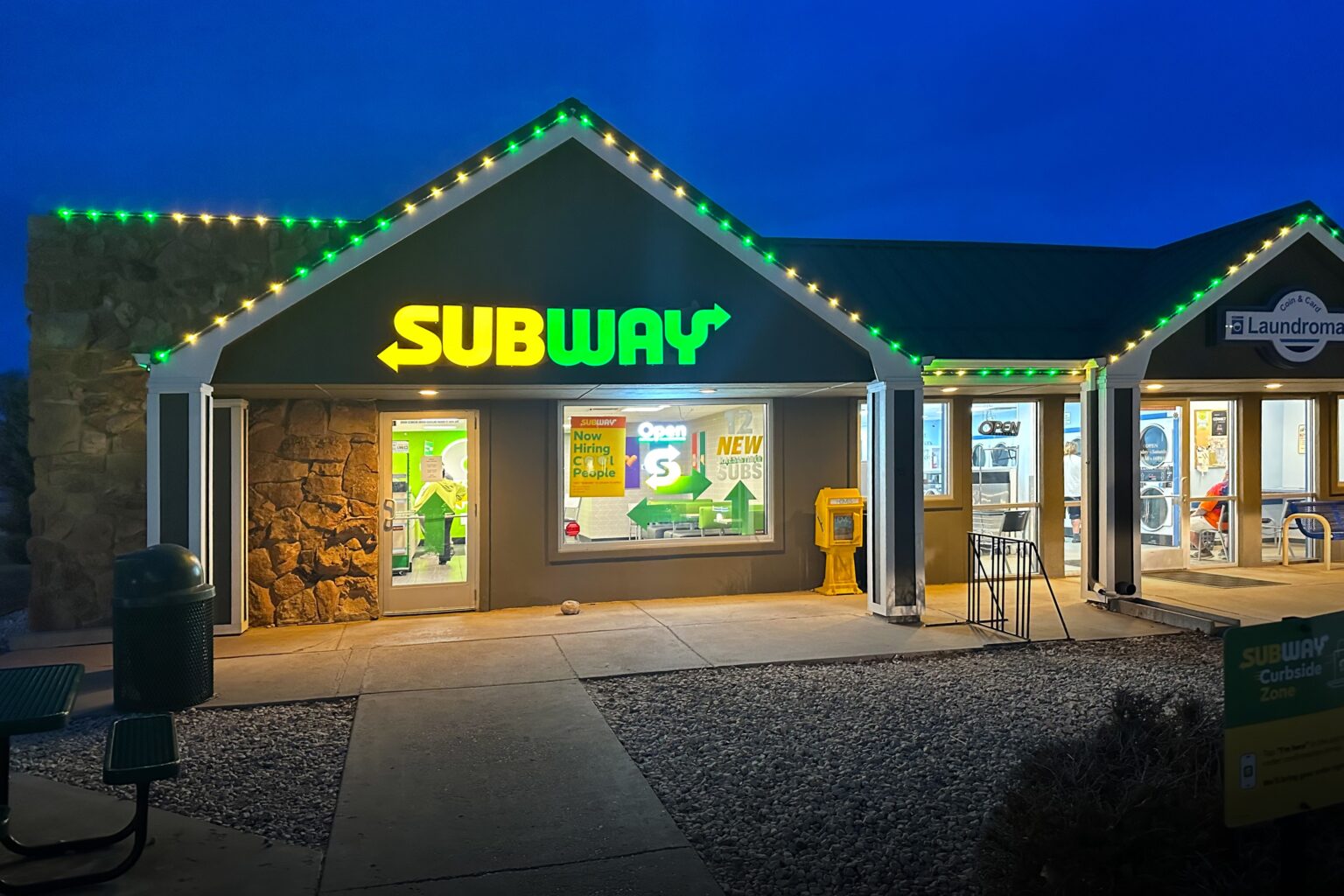 Subway restaurant with green and white decorative trim lighting on the roofline, highlighting the storefront.