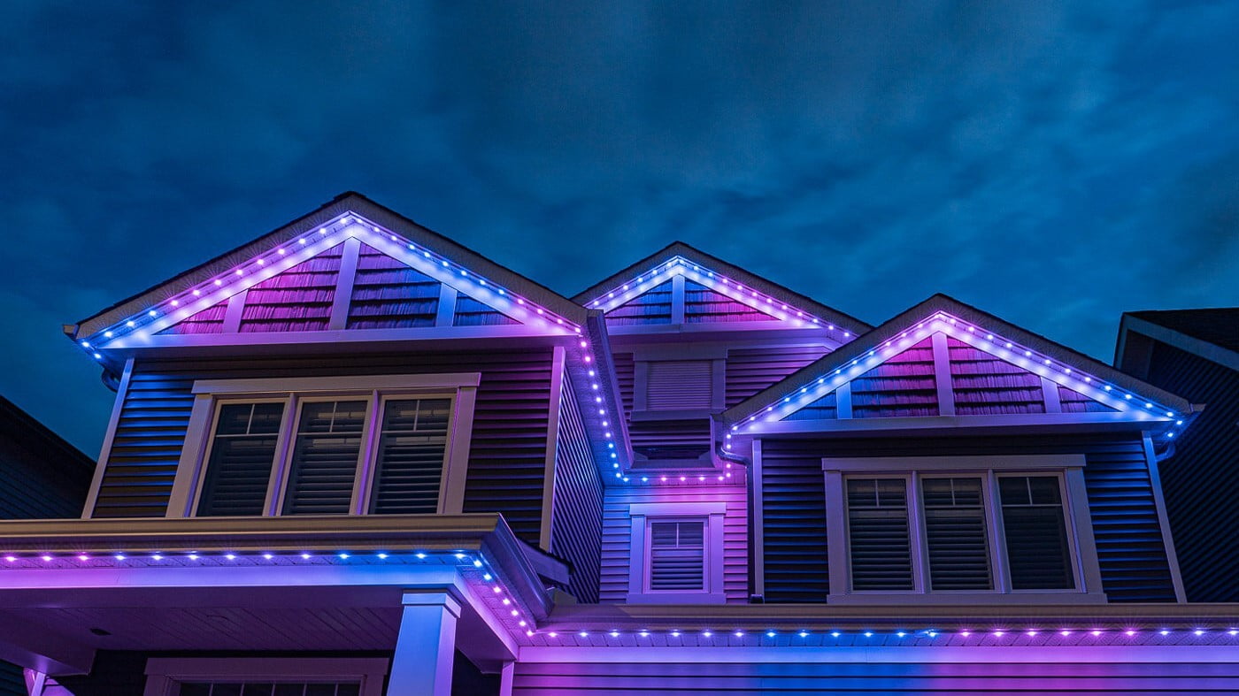 House with vibrant blue and purple permanent trim lights, highlighting the roofline and architectural features.