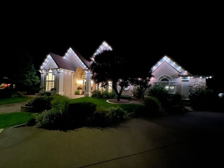 White house with warm white accent lighting on the trim of the gables