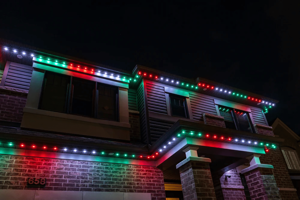 Brick house with red, white, and green permanent Christmas lights shining down the exterior walls