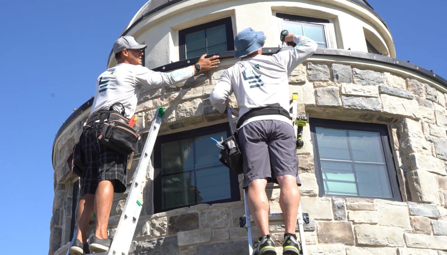 Leading Edge installation technicians on ladders installing permanent trim lighting on a home turret
