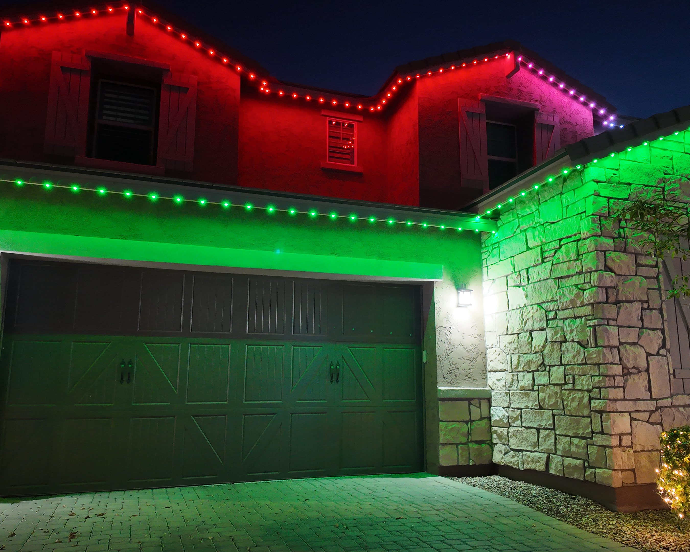 A house with permanent holiday lights in red, green, and purple along the roofline, glowing vibrantly at night.