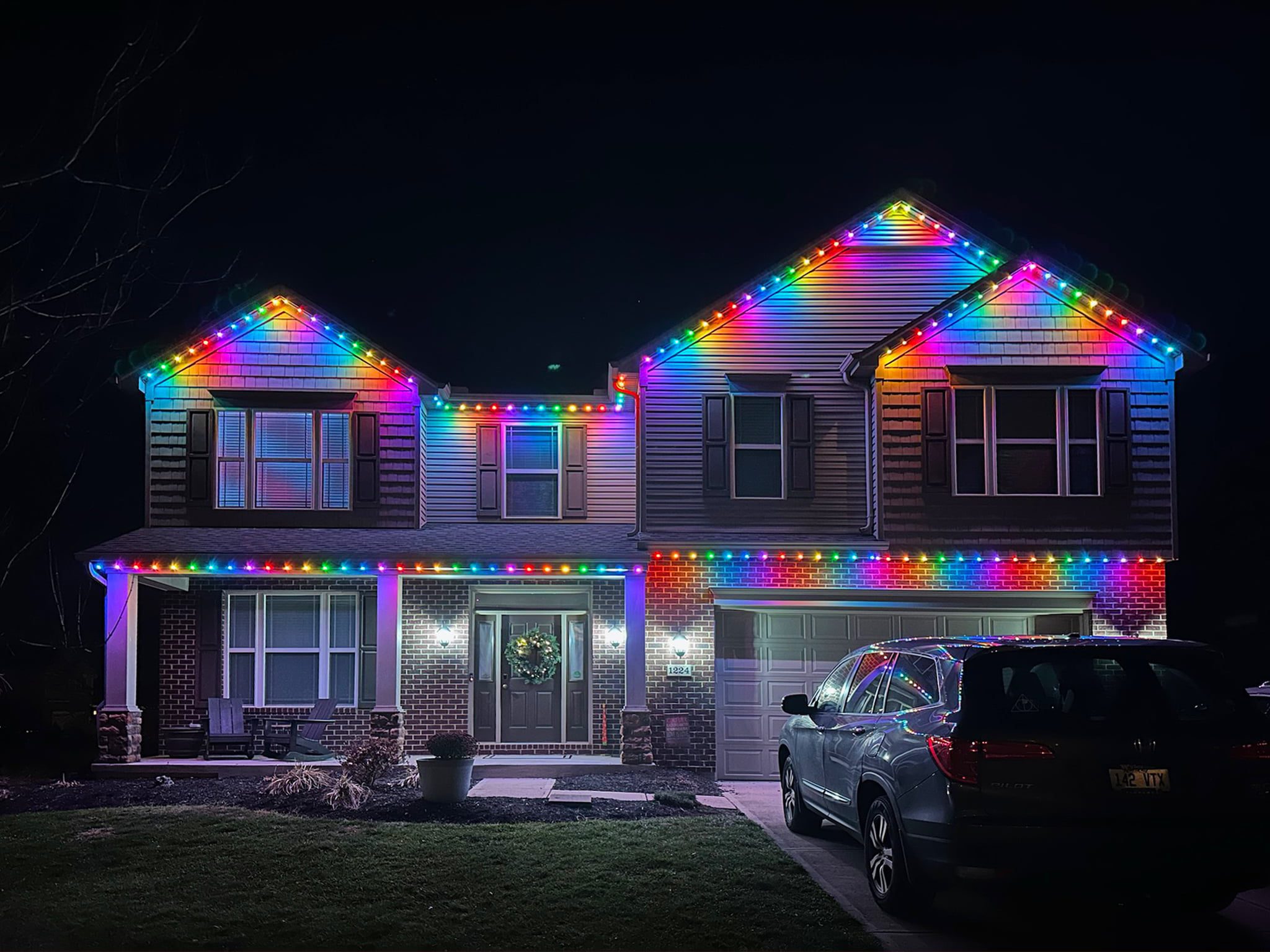 House with vibrant, rainbow-colored permanent holiday lights outlining the roof and windows, creating a festive and joyful atmosphere