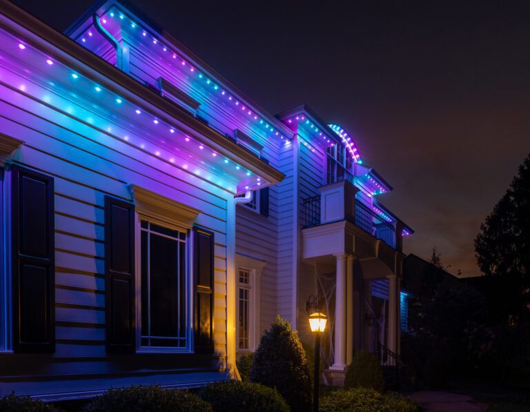 A house with vibrant purple and blue permanent holiday lights illuminating the roofline and architectural details at night.