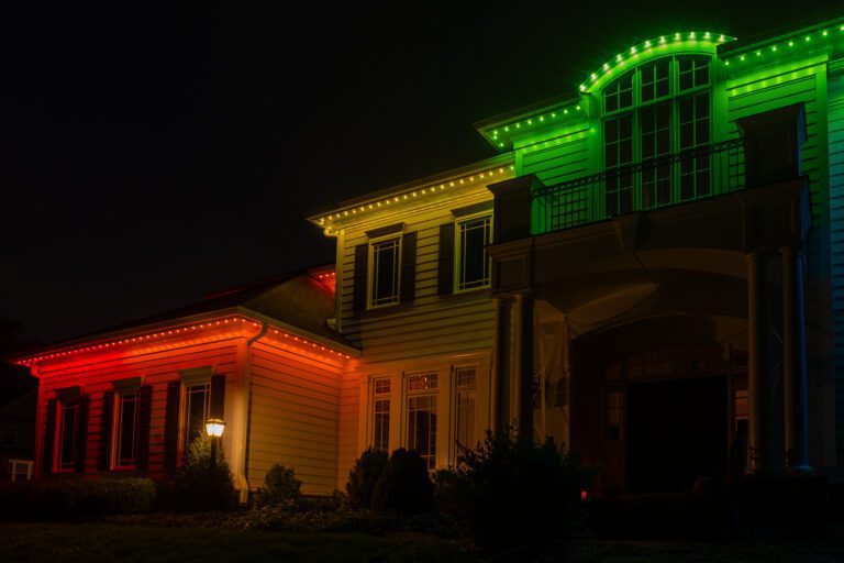 Permanent roofline lighting in festive red, yellow, and green hues illuminating a stunning home.