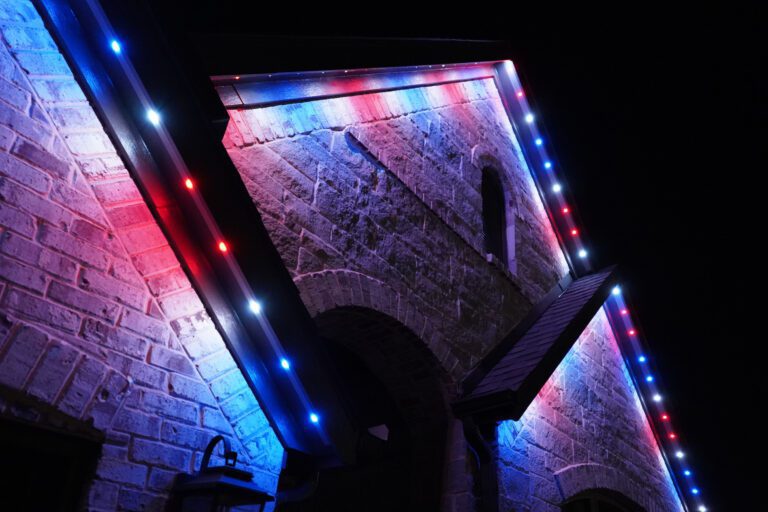 Permanent trim lighting in red, white, and blue illuminating a stone home exterior.