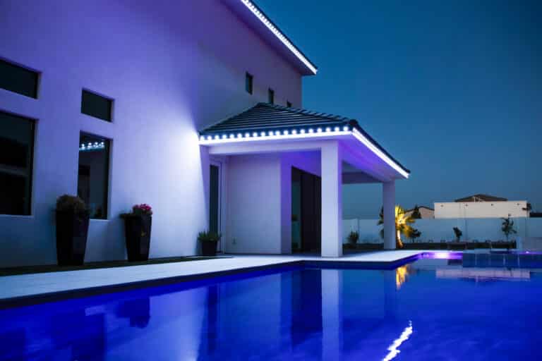 Modern Arizona home with permanent LED trim lighting in cool white and violet tones illuminating covered patio and pool at dusk