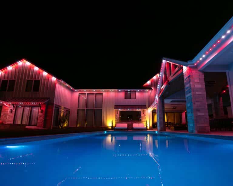 Luxury backyard pool and patio illuminated with permanent LED roofline lighting in red and white colors at night