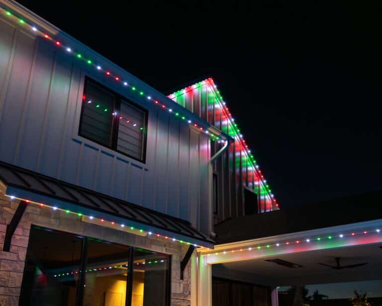 Modern luxury home with professional permanent outdoor lighting displaying red, green, and warm white holiday colors at night