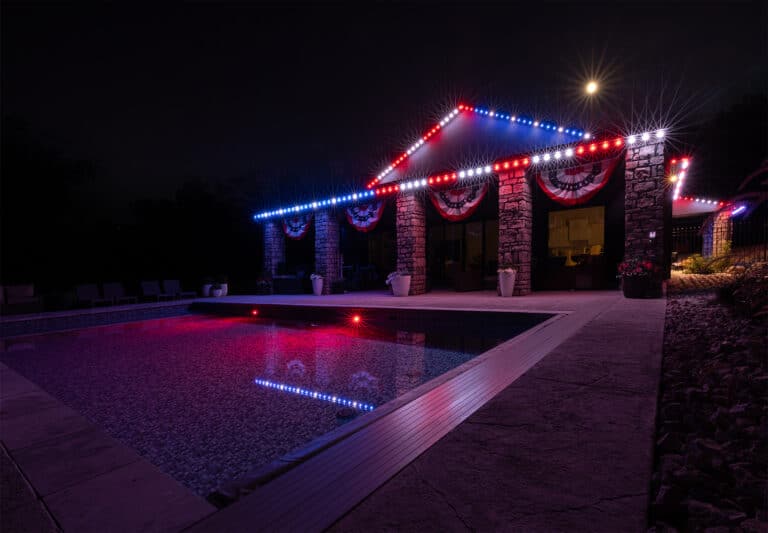 Luxury outdoor patio and pool area illuminated with red white and blue permanent outdoor lighting at night
